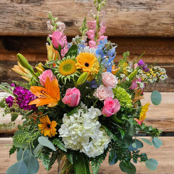 Colorful mixed bouquet in a glass vase with roses, lilies, hydrangea, and gerbera daisies