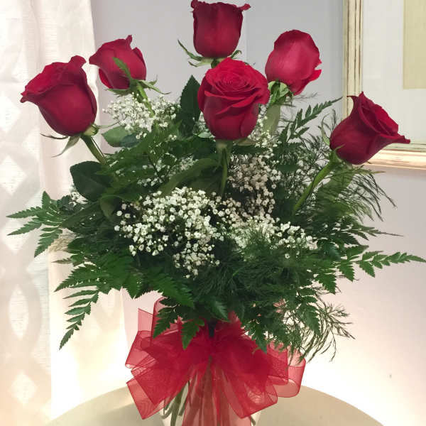 Red roses in a clear vase with baby's breath and a red ribbon