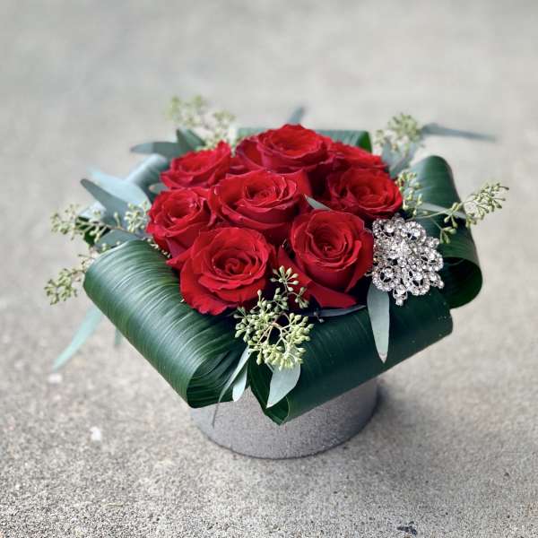 Red roses arranged in a low box with a jeweled brooch accent