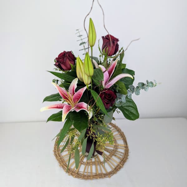 Bouquet of pink lilies and dark red roses with greenery in a woven base