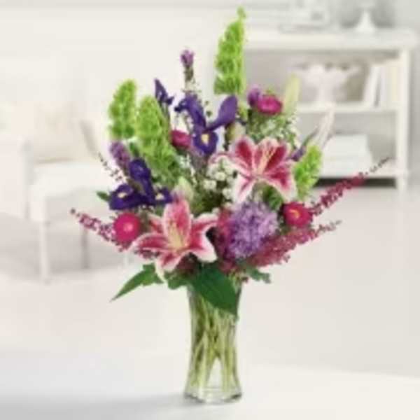 Mixed bouquet of pink lilies and purple flowers in a clear glass vase