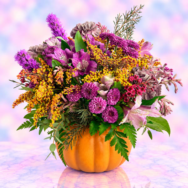 Mixed purple and pink flowers arranged in an orange pumpkin container