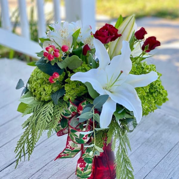 Bouquet with white lilies, red roses, and green hydrangeas in a ribbon-wrapped vase