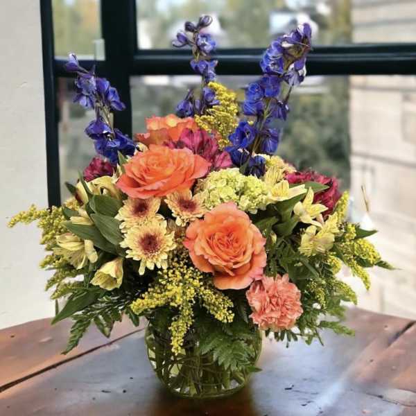 Mixed bouquet of orange, purple, and yellow flowers in a glass vase