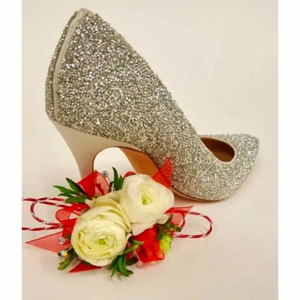 White floral corsage beside a pair of glittery silver high heels
