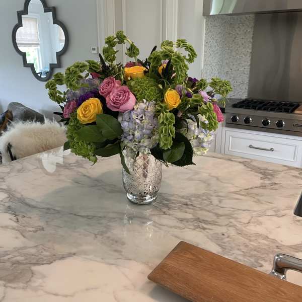 Mixed bouquet of pink, yellow, and lavender flowers in a glass vase