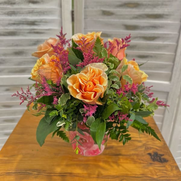 Orange roses in a pink glass vase with magenta filler flowers