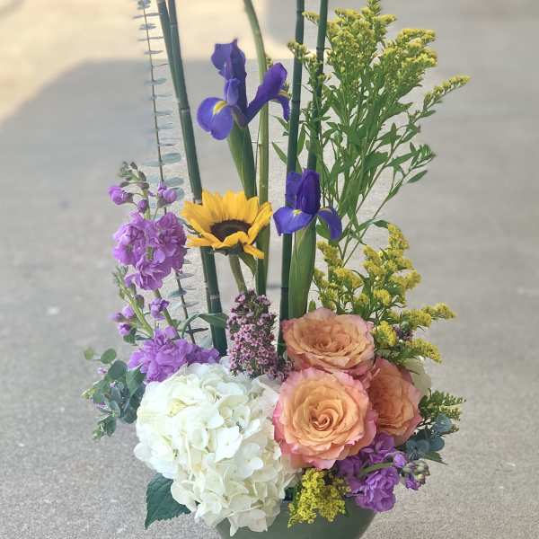 Mixed floral arrangement in a green vase with sunflowers, irises, roses, and hydrangea