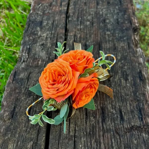 Orange rose corsage with green foliage and gold ribbon on weathered wood