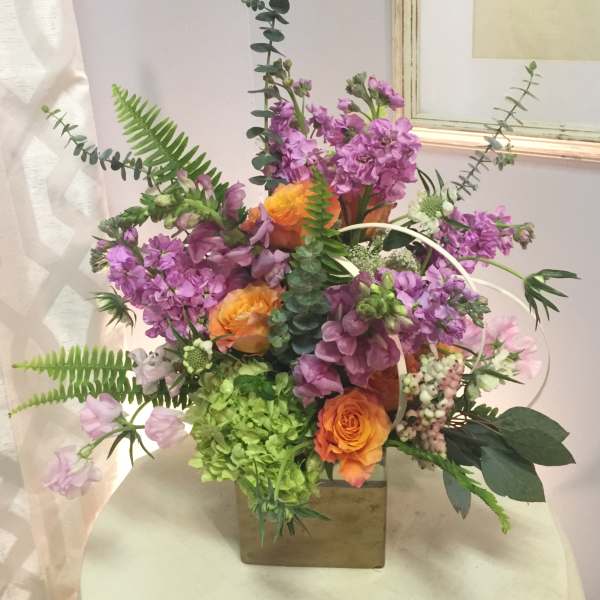 Mixed bouquet with purple flowers and orange roses in a square vase