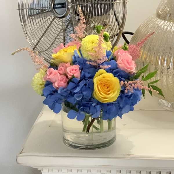 Bouquet of blue hydrangeas, pink roses, and yellow roses in a glass vase