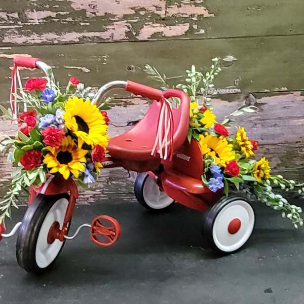 Flower-covered red tricycle with sunflowers and mixed blooms