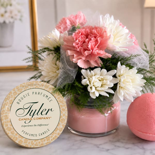 Pink and white flower arrangement in a glass vase with a candle tin and bath bomb