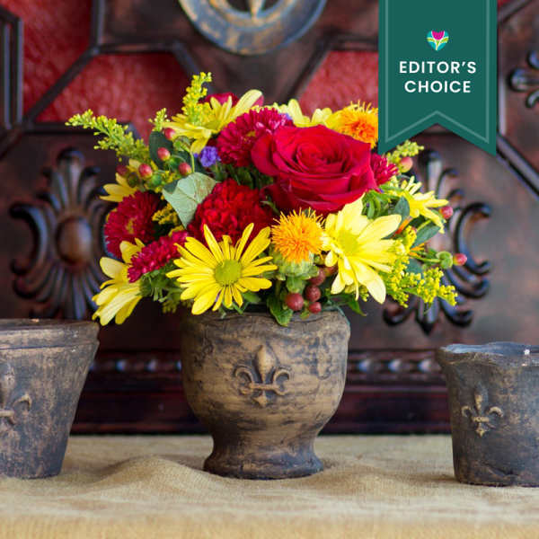 Mixed bouquet of red, yellow, and orange flowers in a rustic vase