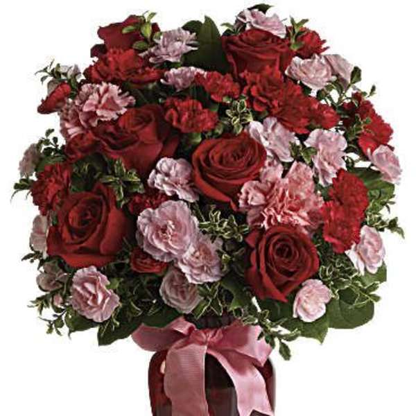 Red roses and pink carnations in a red vase with a pink ribbon