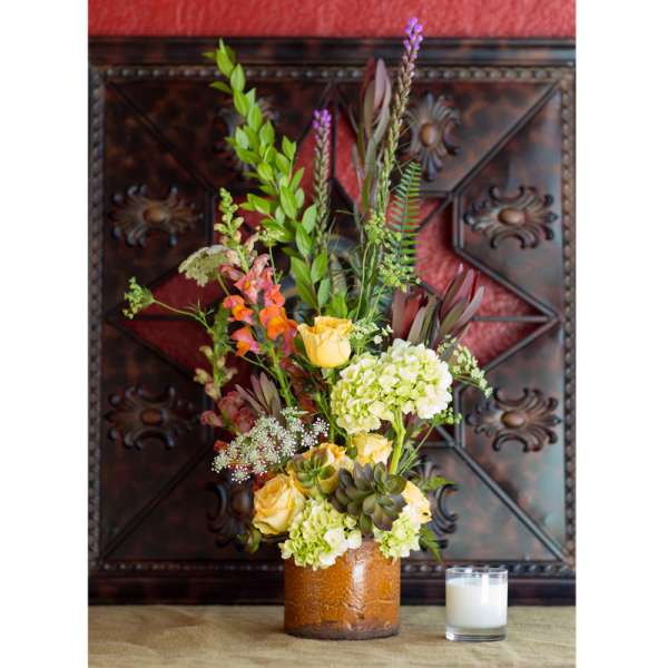 Tall floral arrangement in a brown vase with yellow roses and green hydrangeas