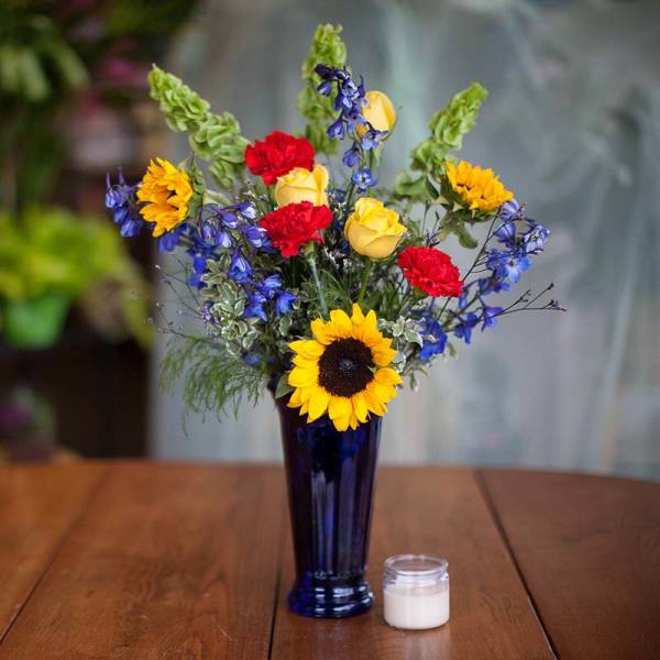 Sunflowers, yellow roses, red carnations, and blue flowers in a tall vase