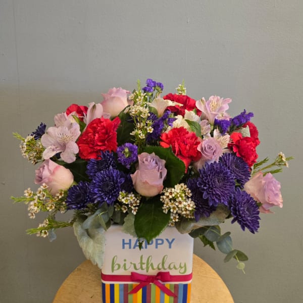 Mixed bouquet of pink, red, and purple flowers in a birthday gift box