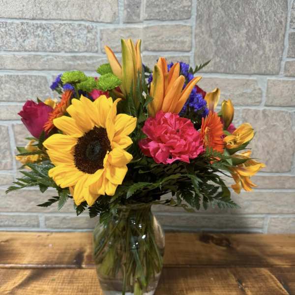 Bright mixed bouquet with sunflowers, lilies, carnations and other blooms in a clear glass vase