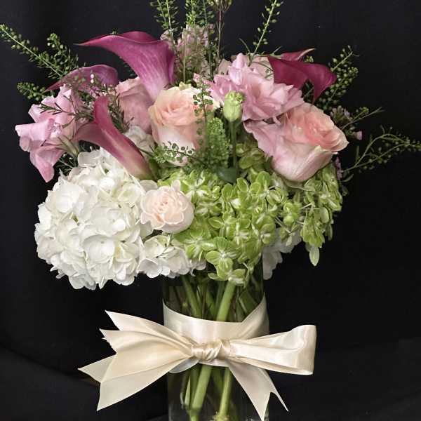 Pink calla lilies and roses in a glass vase with a cream ribbon
