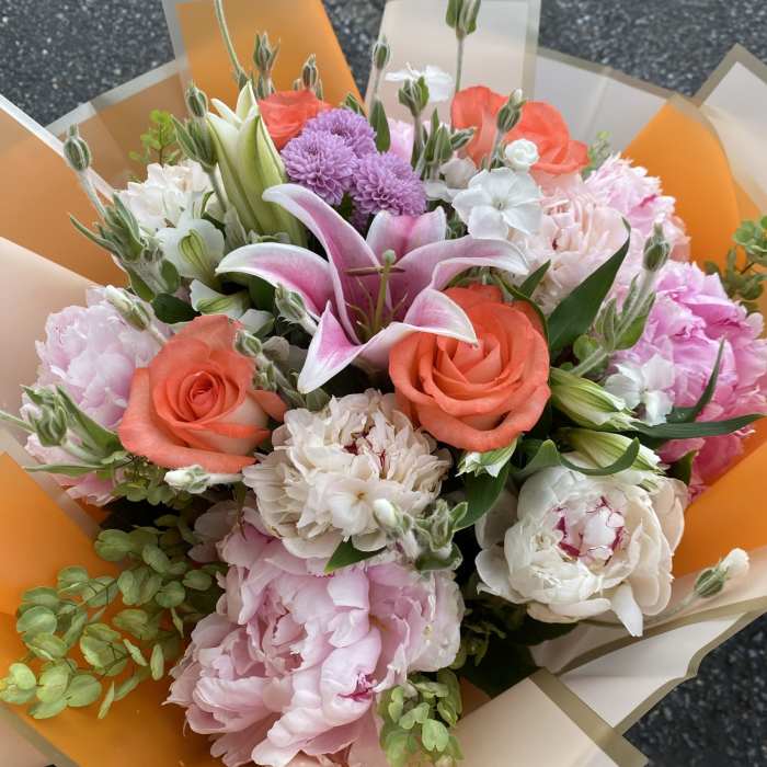 Mixed bouquet with pink lilies, coral roses, and white blooms wrapped in orange paper