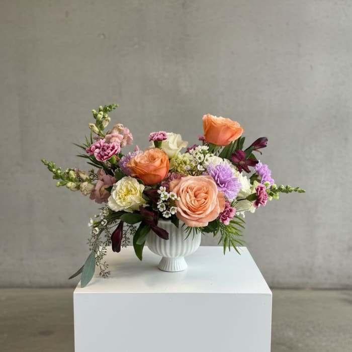 Mixed bouquet of peach, pink, and white flowers in a white vase