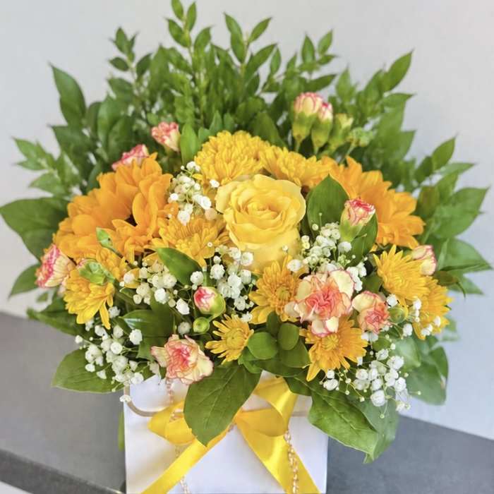 Yellow and orange flower arrangement in a white box with a yellow ribbon