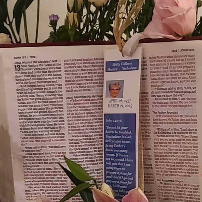Floral memorial display with pink lilies, cream roses, and an open Bible