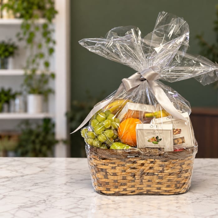 Gift basket with grapes, an orange, and packaged snacks in a wicker basket