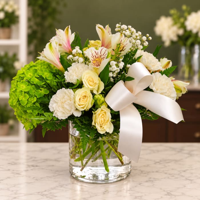 White and cream bouquet with lilies, roses, and carnations in a glass vase