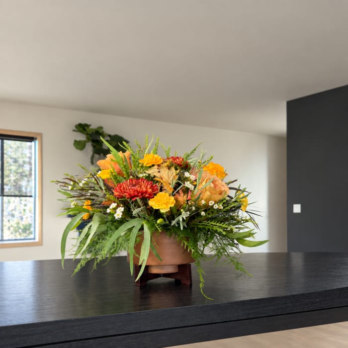 Mixed orange, yellow, and red flowers arranged in a low bowl on a stand