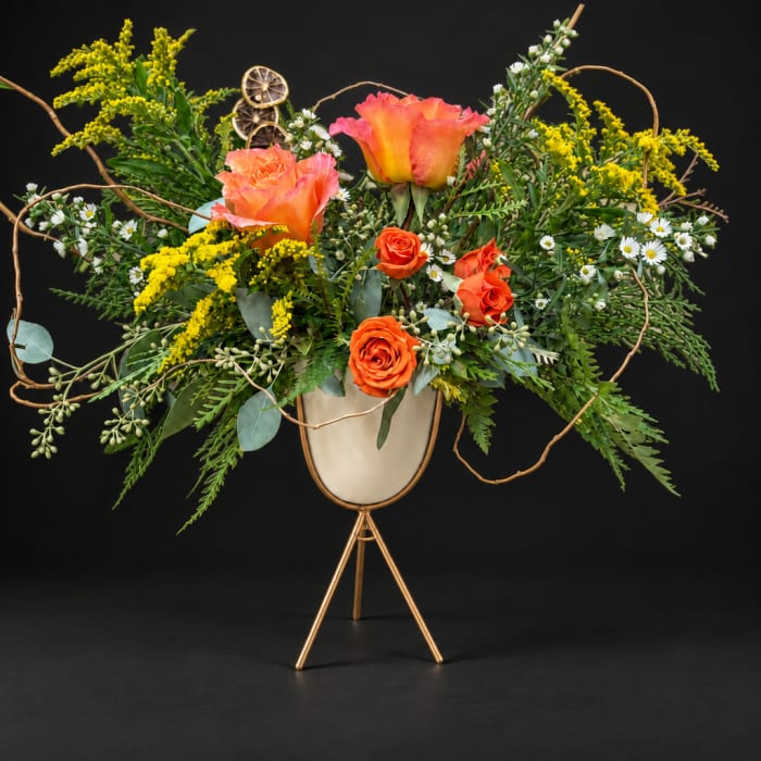 Orange roses and yellow flowers in a gold stand vase