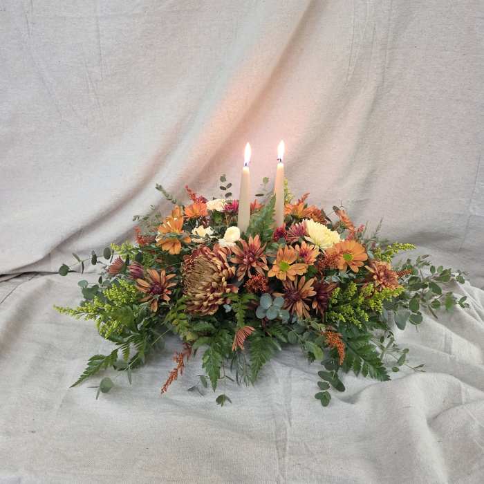 Low autumn centerpiece of orange and yellow mums with two lit ivory taper candles
