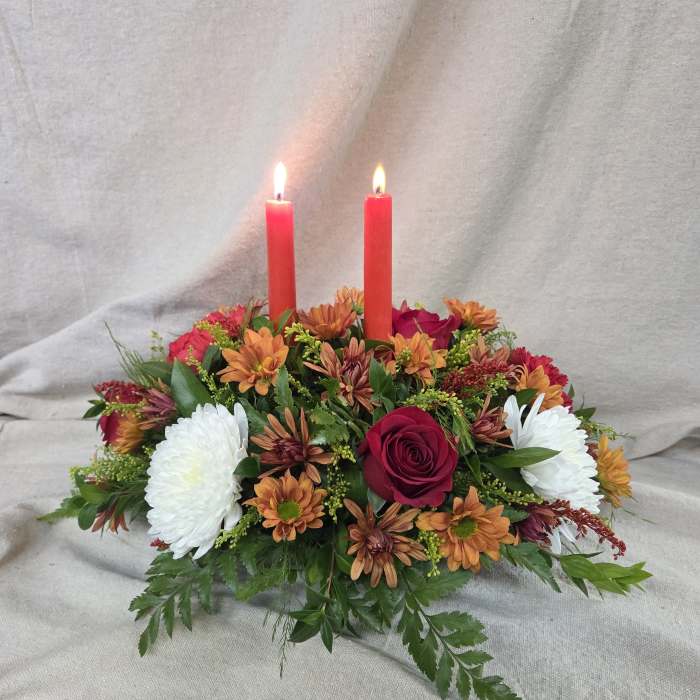 Low centerpiece with red candles, red roses, orange mums, and white mums in an oval design