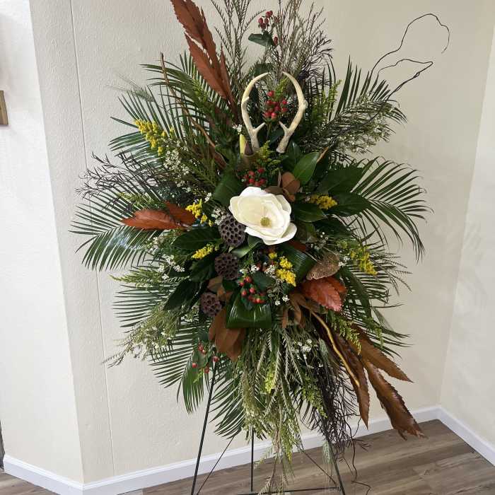 Tall floral standing spray with white bloom and mixed greenery on an easel