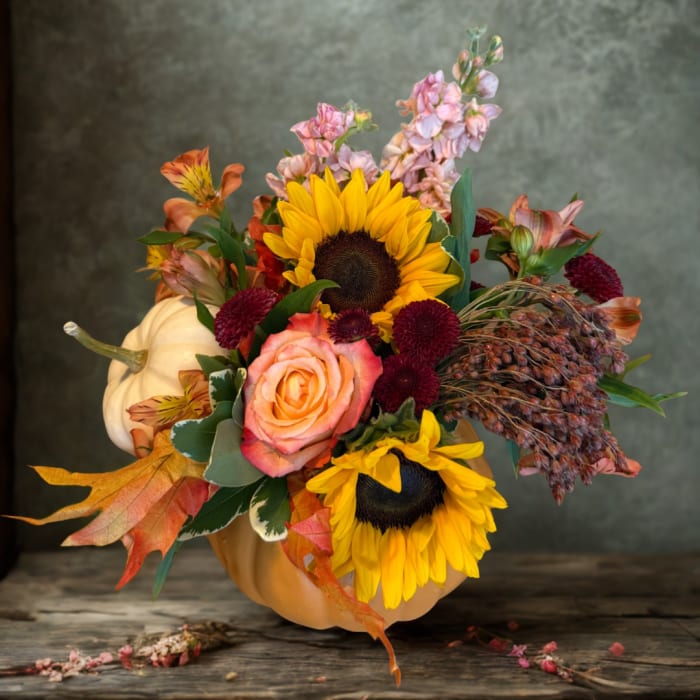 Fall floral arrangement in a pumpkin container with sunflowers and roses