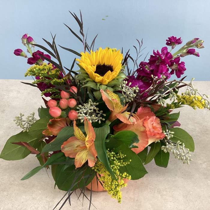 Mixed bouquet with a sunflower, pink blooms, and peach flowers in a low container
