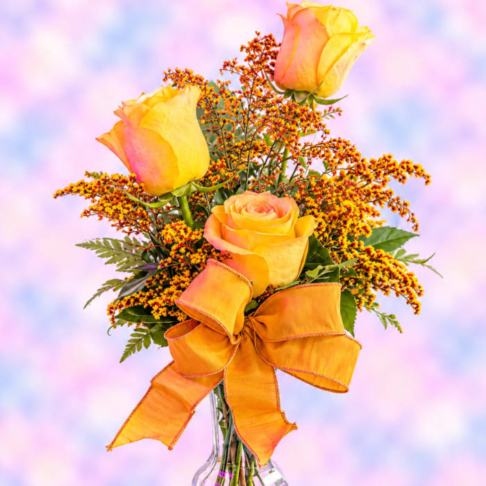 Yellow and peach roses in a glass vase with an orange bow