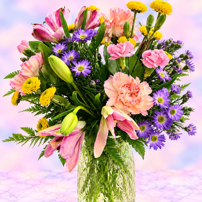 Mixed bouquet of pink lilies, carnations, and purple daisies in a glass vase