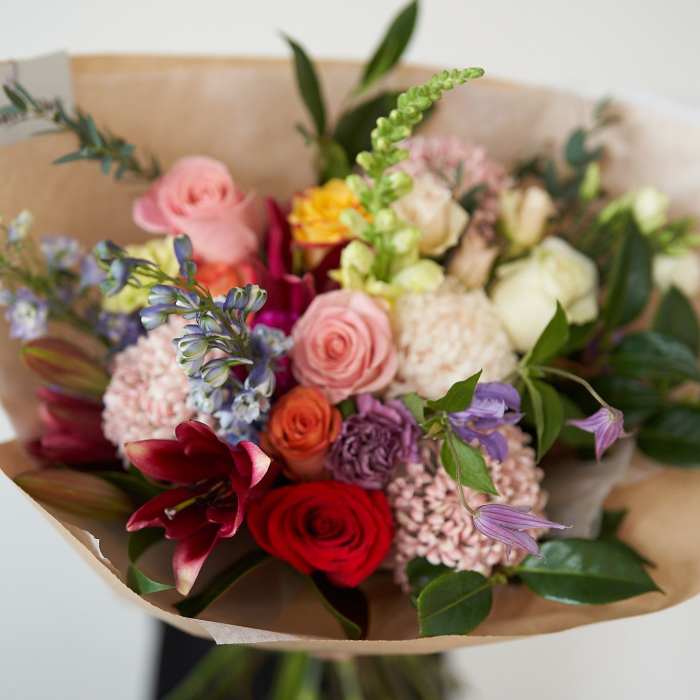 Mixed bouquet of roses, lilies, and purple flowers wrapped in brown paper