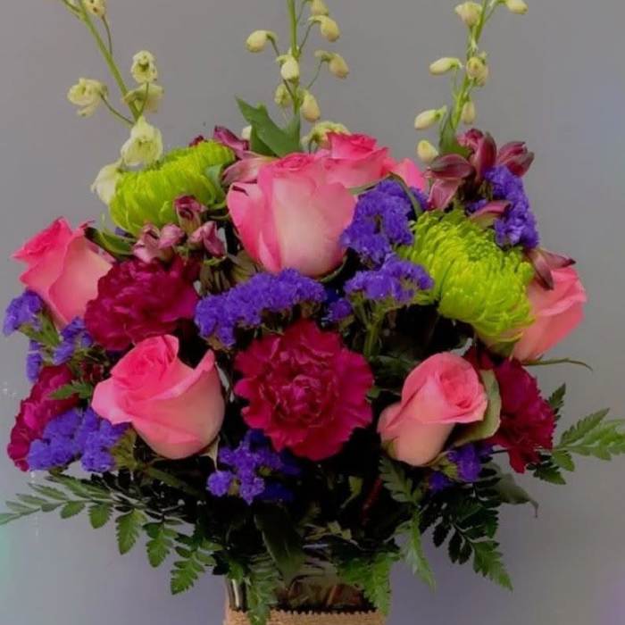 Pink roses and purple flowers arranged in a glass vase with burlap wrap