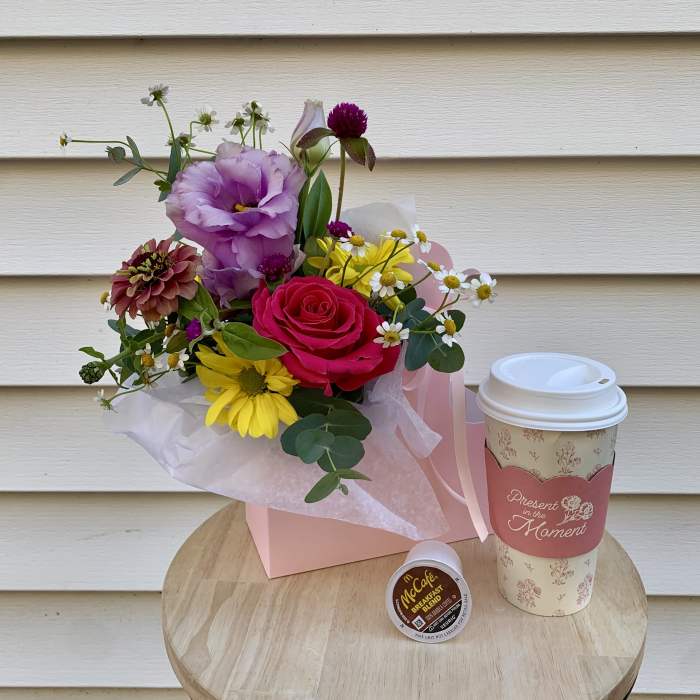 Mixed bouquet in a pink box with a coffee cup and coffee pod beside it