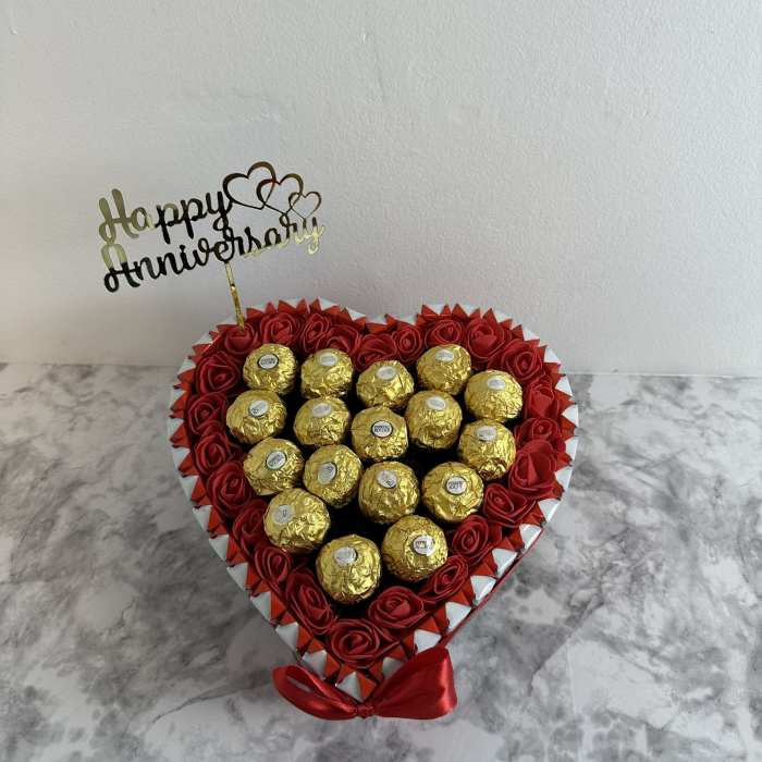 Heart-shaped box of red roses and gold-wrapped chocolates with a Happy Anniversary topper