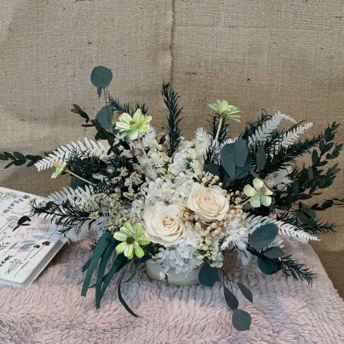 White and cream floral arrangement with dark green foliage in a low vase