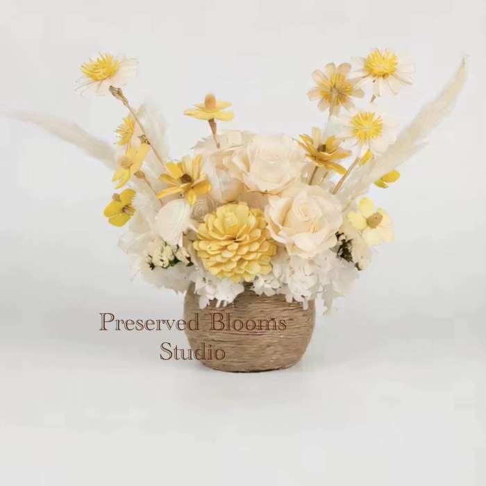 Yellow and cream preserved flower arrangement in a small woven basket container