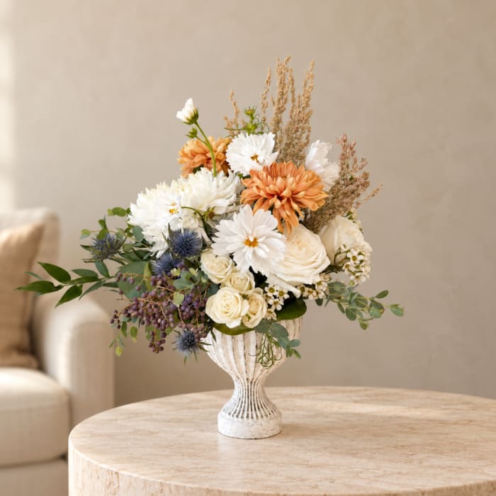 White and peach floral arrangement in a white pedestal vase