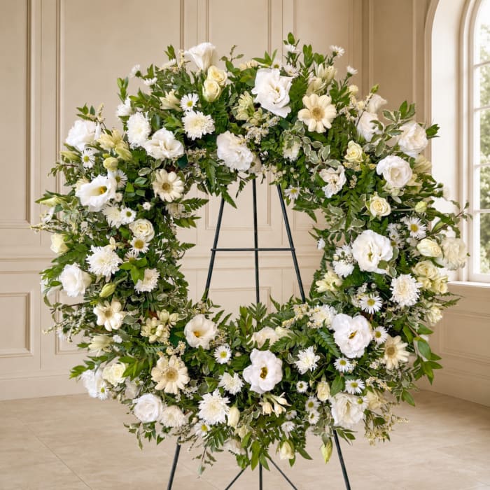 Large white floral wreath on a black stand in a bright room