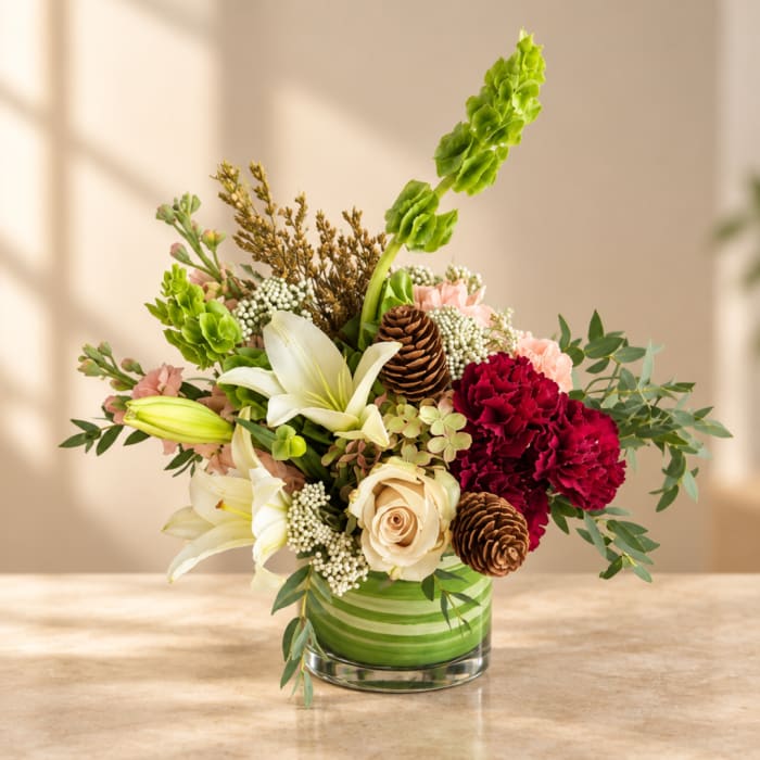 Mixed floral arrangement in a green striped glass vase with lilies and carnations