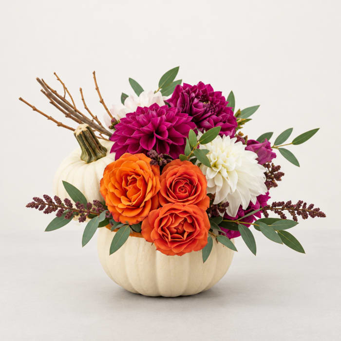 Orange and magenta flowers arranged in a white pumpkin vase