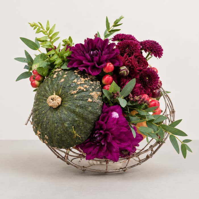 Purple flowers arranged with a green pumpkin in a wire basket